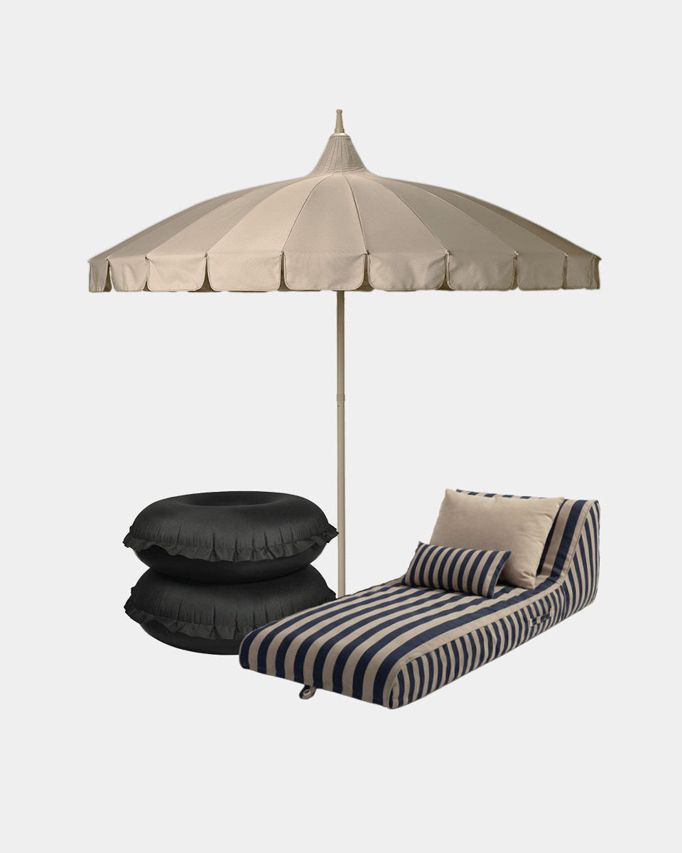 Outdoor patio furniture set including a beige patio umbrella, a black and beige striped lounge with matching pillows, and two black pool rings, isolated on a light gray background.