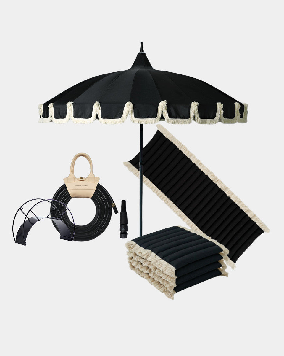 Black patio umbrella set with cream fringed trim, shown with a black garden hose, black and cream white seat and bench cushions on a light gray background.