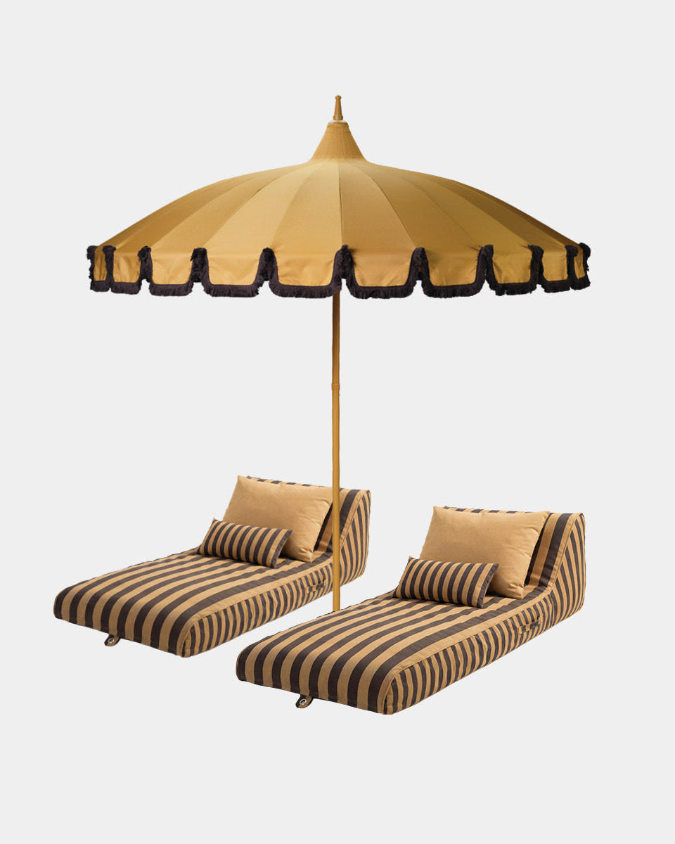 A luxury outdoor patio set featuring two modern sun lounge with vertical brown and saffron stripes, matching pillows, and a large matching saffron and brown parasol umbrella on a light gray background.