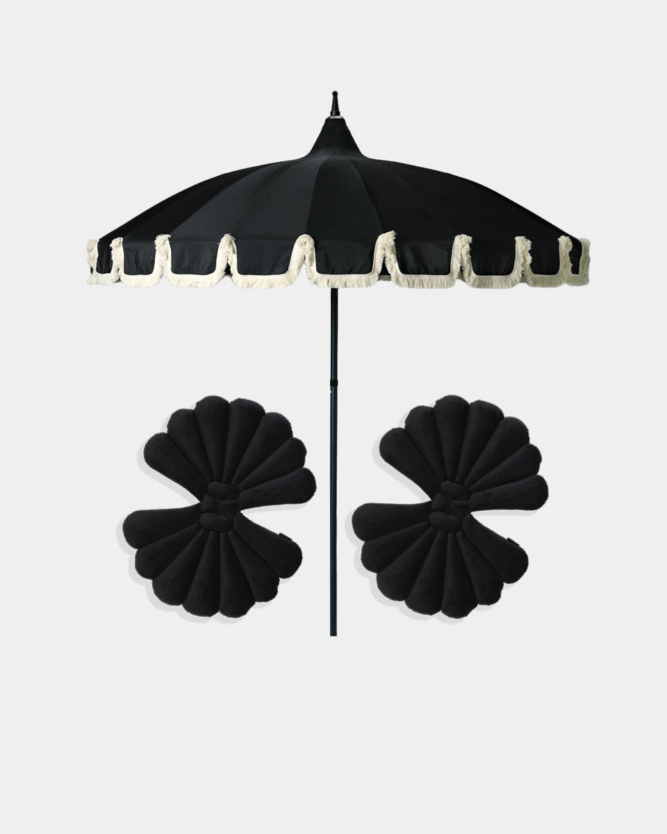 A black umbrella with a cream-colored fringed trim, shown open with two matching black flower-shaped accessories below it, all set against a solid light gray background.
