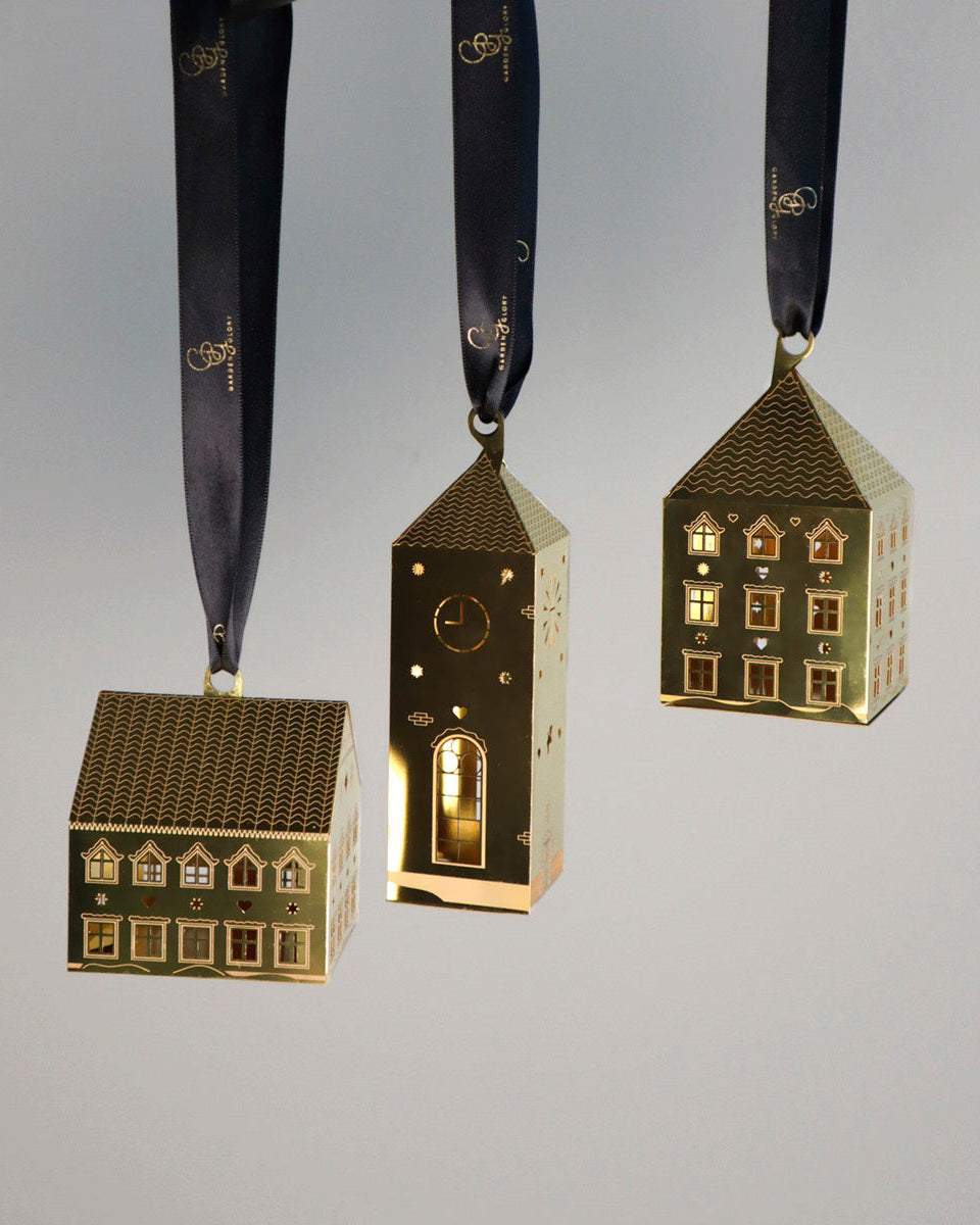 Three gold house-shaped ornaments on ribbons against a gray background