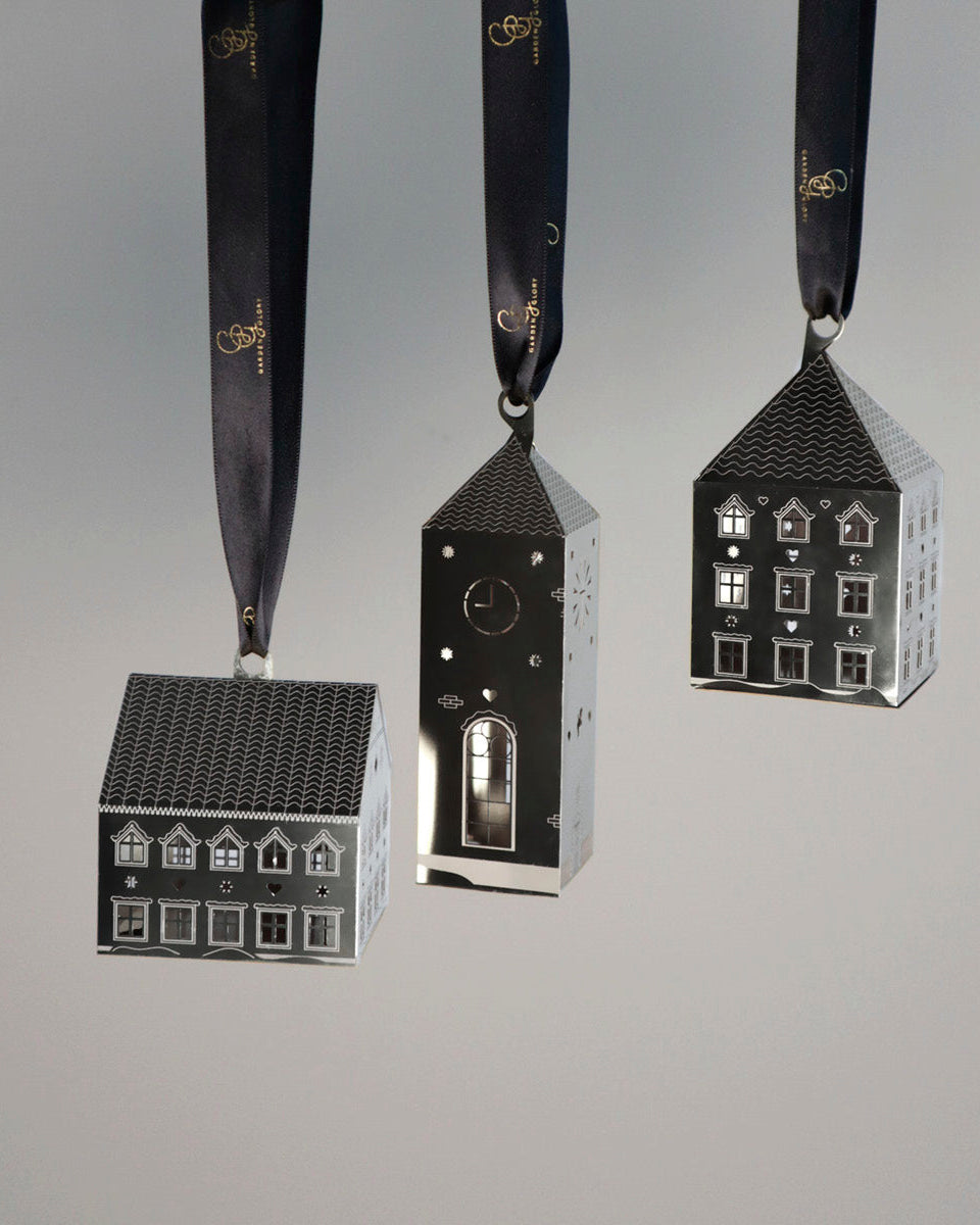 Three house-shaped ornaments on ribbons against a gray background
