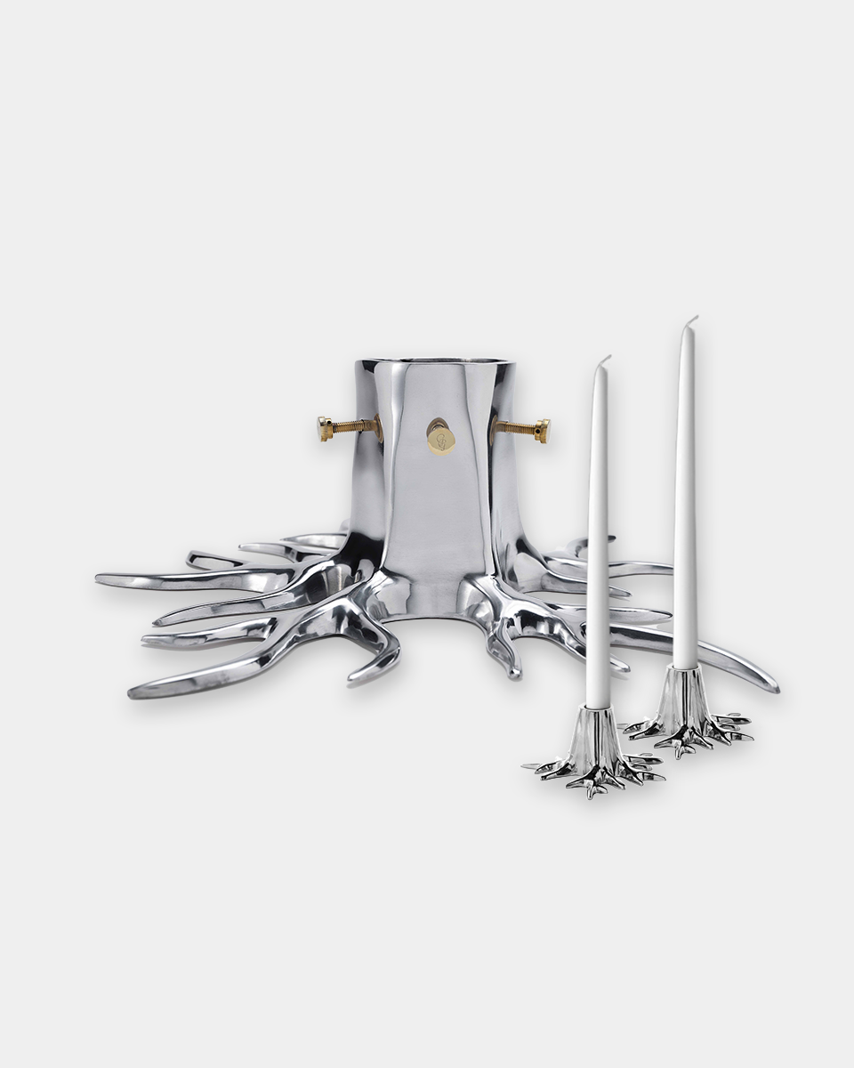 A polished silver-toned metal candle holder shaped like tree roots or branches, with two matching candlesticks placed in front, photographed on a clean light gray background.