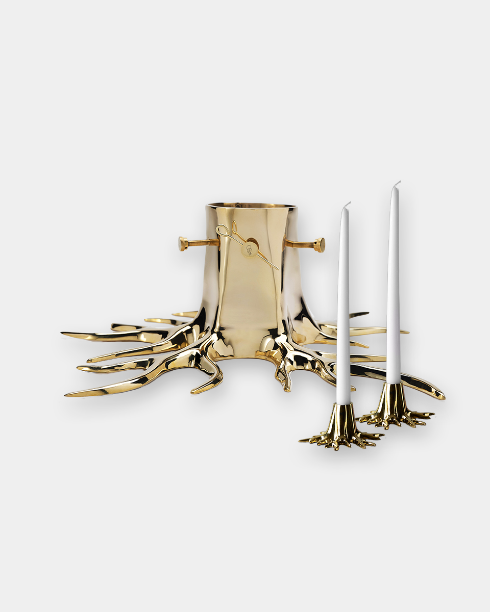 A gold tree stump candle holder with three white taper candles on a light gray background.